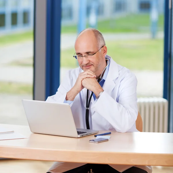 Arzt mit Hand am Kinn und Laptop — Stockfoto