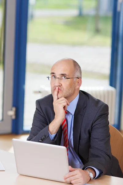 Empresario con portátil mirando hacia arriba en el escritorio — Foto de Stock