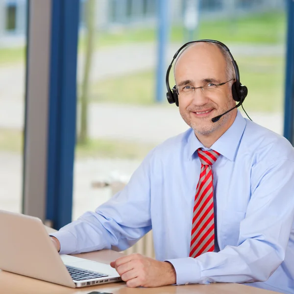 Männlicher Kundendienstleiter trägt Kopfhörer, während er Lapt benutzt — Stockfoto