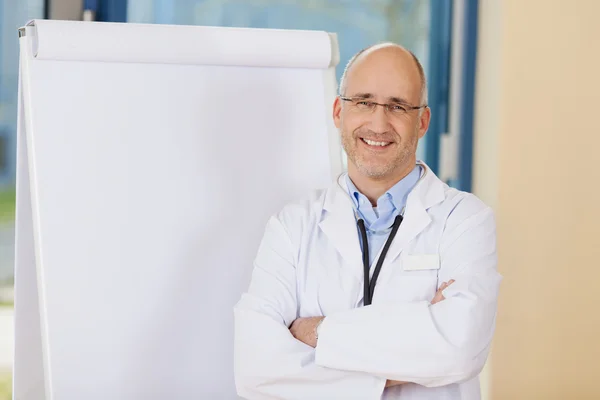 Arzt mit verschränkten Armen im Stehen am Flipchart — Stockfoto