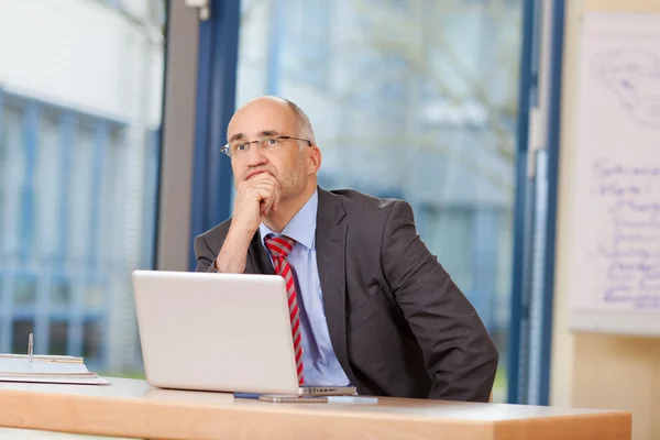 Uomo d'affari con mano sul mento guardando lontano alla scrivania — Foto Stock