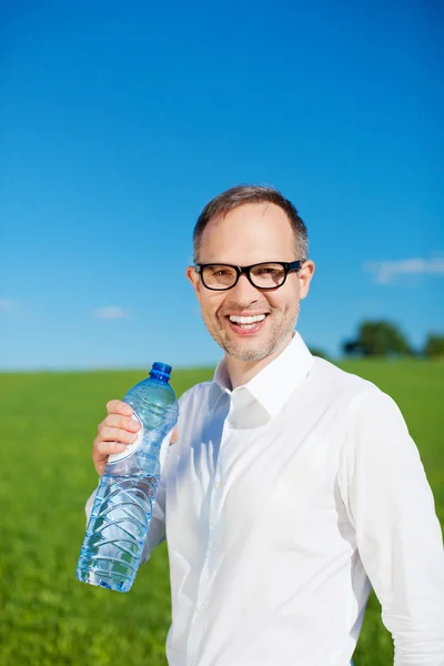 Man standing in a green field drinking water — Stock Photo, Image