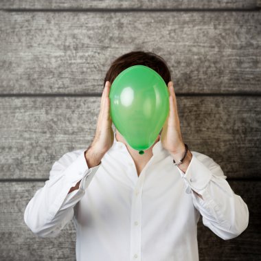 Businessman Holding Balloon In Front Of Face Against Wooden Wall clipart