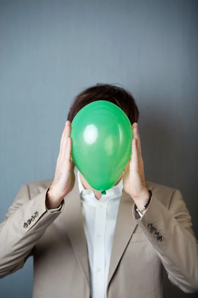 Empresário segurando balão na frente da cara contra a parede azul — Fotografia de Stock