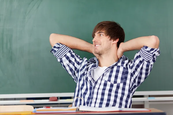 Estudiante masculino relajándose en el escritorio contra pizarra —  Fotos de Stock
