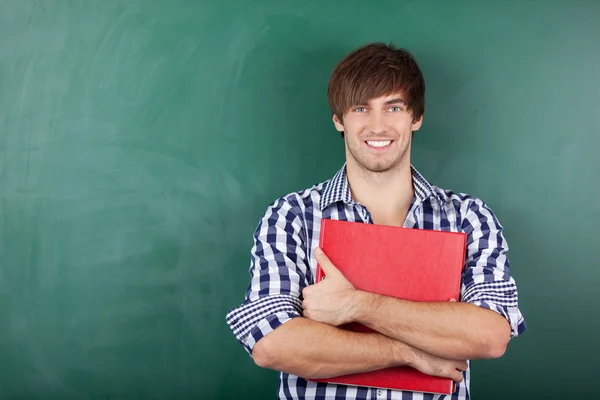 Estudante masculino com ligante vermelho em pé contra Chalkboard — Fotografia de Stock