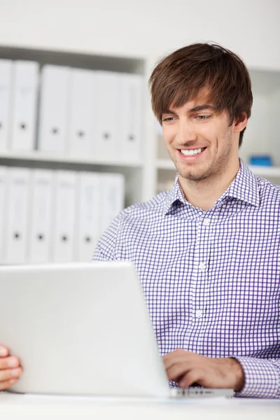 Homme souriant utilisant un ordinateur portable dans le bureau — Photo