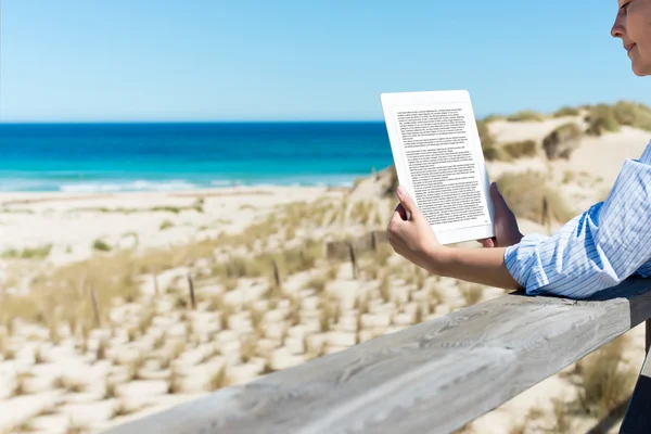 Donna che legge E-Reader alla recinzione sulla spiaggia — Foto Stock