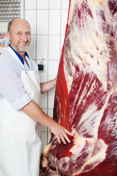 Happy butcher near a hanging cow carcass — Stock Photo, Image
