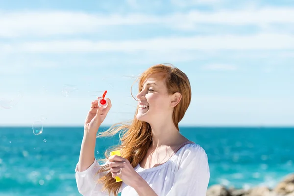 Woman blowing bubbles at the sea — Stock Photo, Image