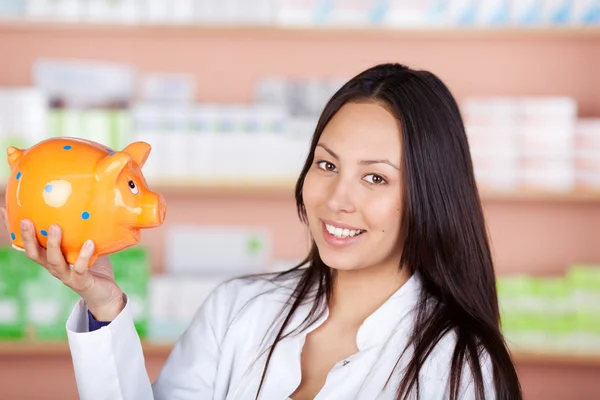 Jovem vendedora em farmácia segurando banco porquinho — Fotografia de Stock