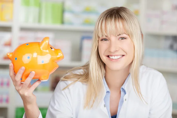 Pharmacist holding piggybank in her hand — Stock Photo, Image