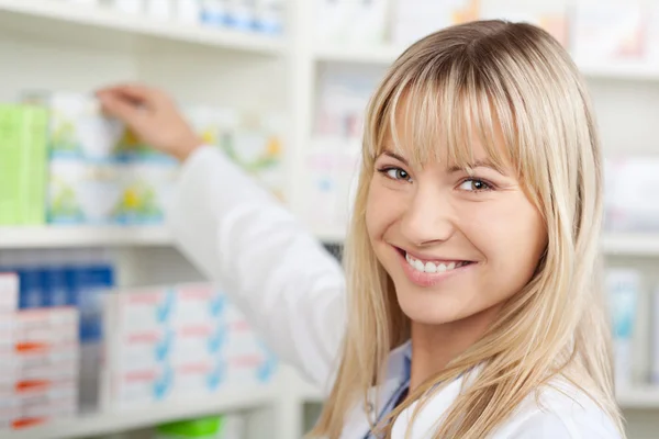 Farmacéutico sonriente tomando medicamentos de la estantería —  Fotos de Stock