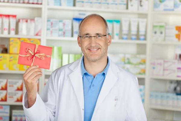 Улыбающийся фармацевт показывает красный купон — стоковое фото