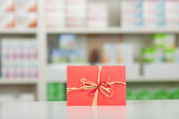 Geschenk verpakt in rood papier en boog bij apotheek balie — Stockfoto