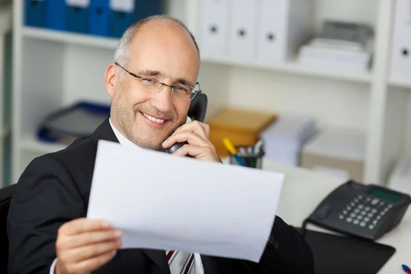 Geschäftsmann liest Dokument beim Telefonieren — Stockfoto