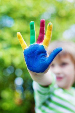 Boy showing his colorful painted hand in the garden clipart