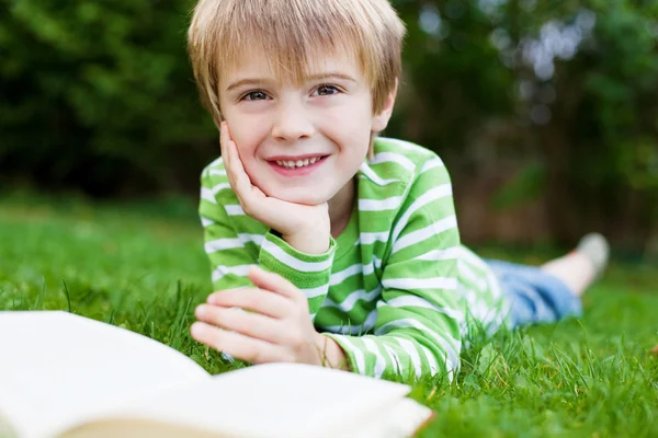 Glimlachend jongen lezing boek in de tuin — Stockfoto