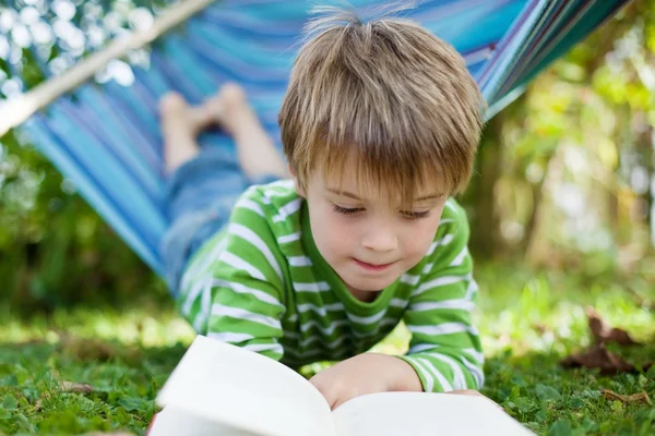 Glad liten pojke läser bok i hängmattan — Stockfoto