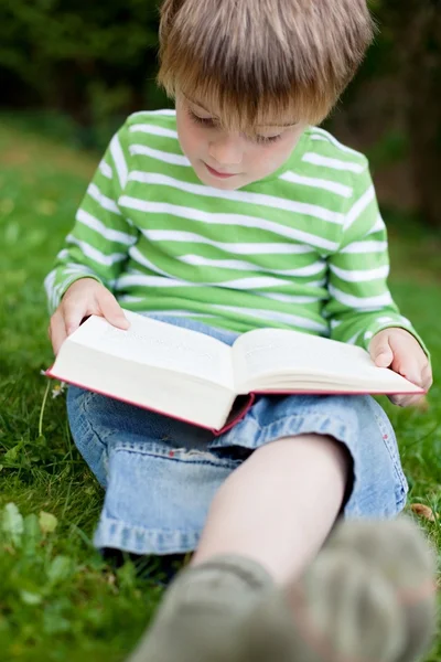 少年は緑の芝生の上に座って読む — ストック写真