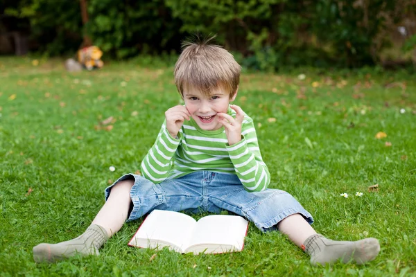 Cheerful little boy reading book on the grass — Stock Photo, Image