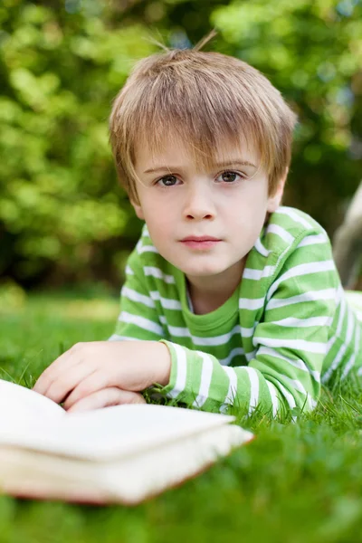 Young boy looking up from reading a book — Stock Photo, Image