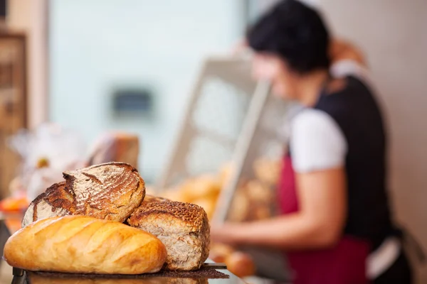 Bread Loafs On Counter With Woman Empting Create In Background — Stock Photo, Image