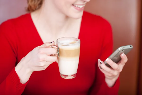 Женщина, использующая мобильный телефон, держа в руках чашку кофе Латте — стоковое фото