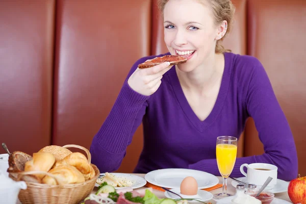 Mujer comiendo rebanada de pan con mermelada en la mesa de café — Foto de Stock