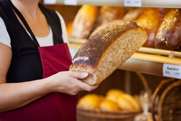 Bäckereiangestellte hält Brotlaib an Vitrine — Stockfoto