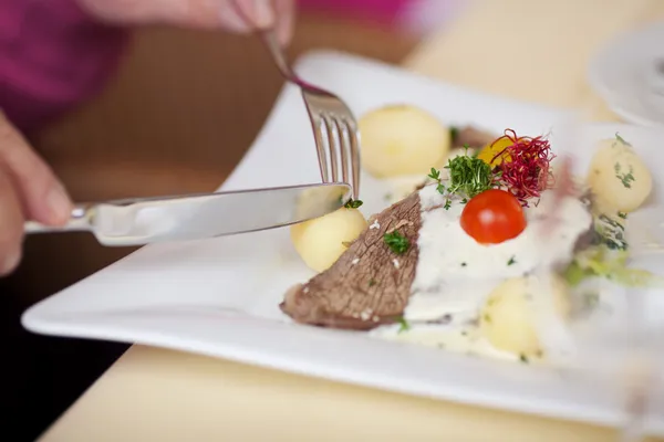 Mãos segurando garfo e faca para cortar batata na mesa — Fotografia de Stock