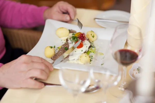 Muž s jídlo drží vidličku a nůž v restauraci u stolu. — Stock fotografie