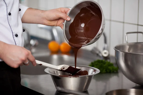 Шеф-повар наливает жидкий шоколад в миску на кухонном столе — стоковое фото