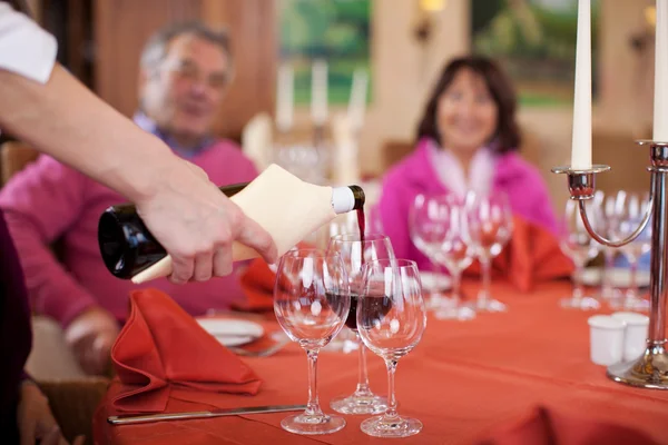 Waitress pouring red wine at guests glasses — Stock Photo, Image