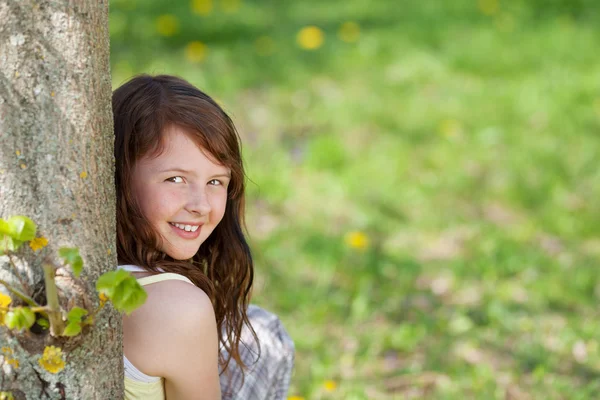 Девушка с закрытыми глазами, опирающаяся на ствол дерева в парке — стоковое фото