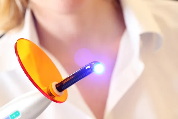 El dentista sostiene una luz UV de curado dental iluminada — Foto de Stock