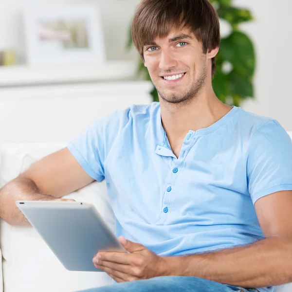 Jeune homme assis sur un canapé travaillant avec une tablette — Photo