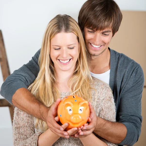 Pareja entre cajas de transporte holding piggybank — Foto de Stock