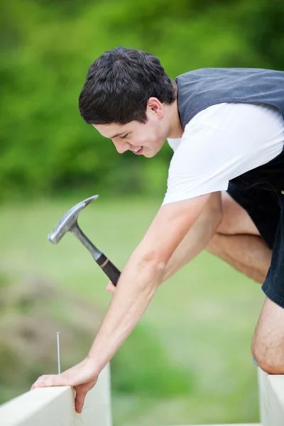 Young carpenter hammering a nail on a beam — Stock Photo, Image