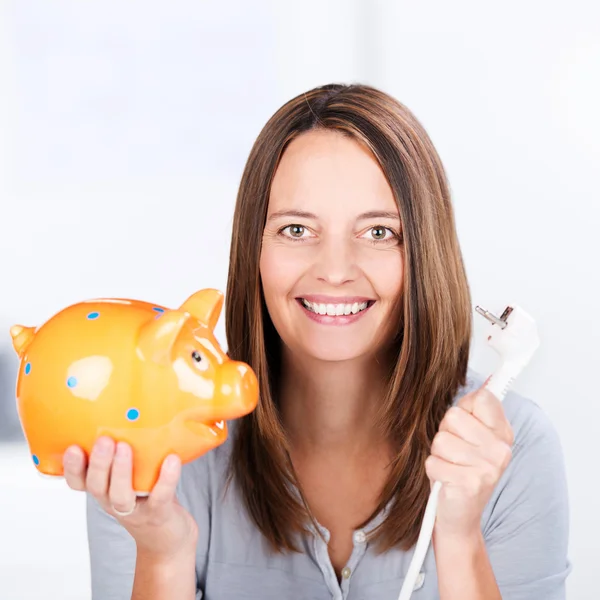 Businesswoman Holding Electric Plug And Piggybank In Office — Stock Photo, Image