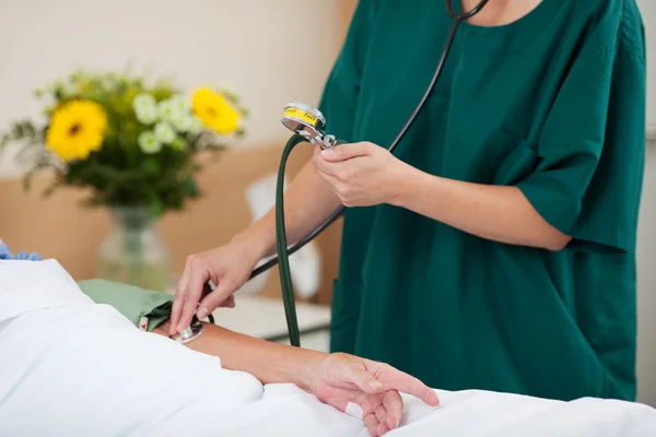 Enfermera midiendo la presión arterial mientras mira el medidor —  Fotos de Stock