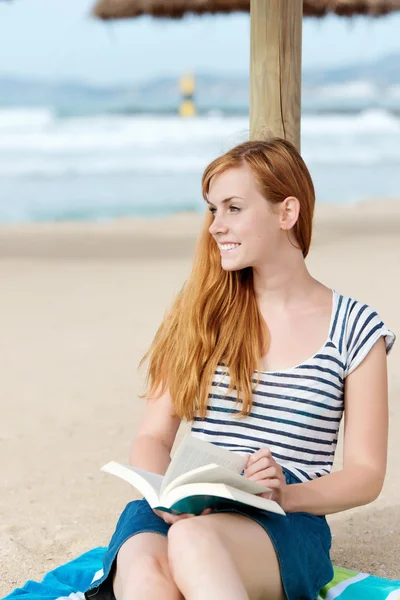 Femme rousse souriante avec livre sur la plage — Photo