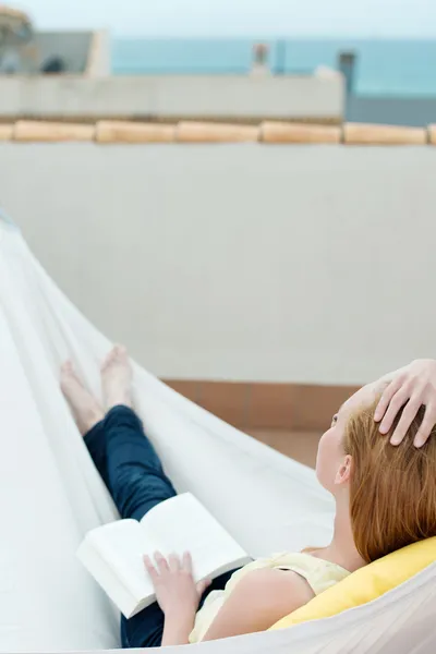 Mulher relaxante com livro em rede — Fotografia de Stock