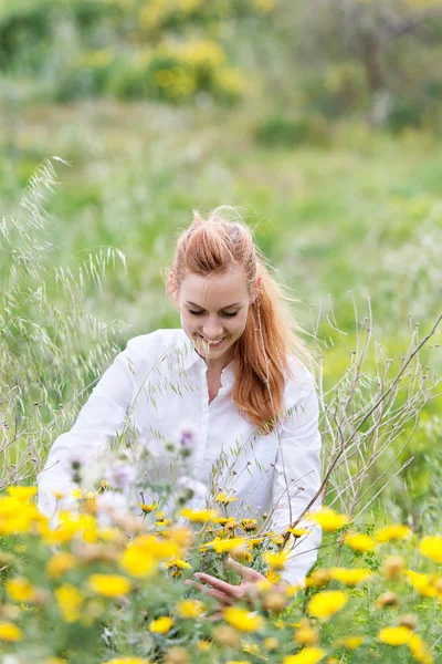 Lachende redhead vrouw die zit te midden van bloemen in veld — Stockfoto