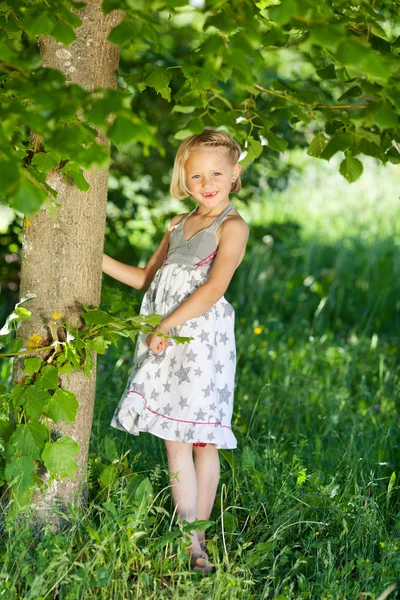 Beautiful little girl under a green tree — Stock Photo, Image