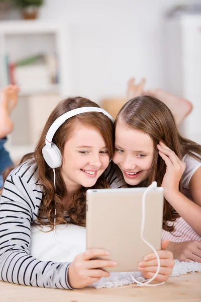 Two young girls share headphones to listen music — Stock Photo, Image