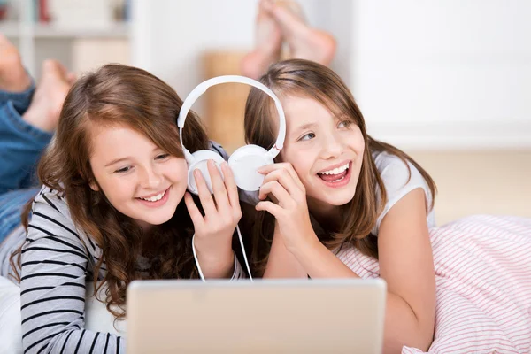 Two young girls share headphones to listen music