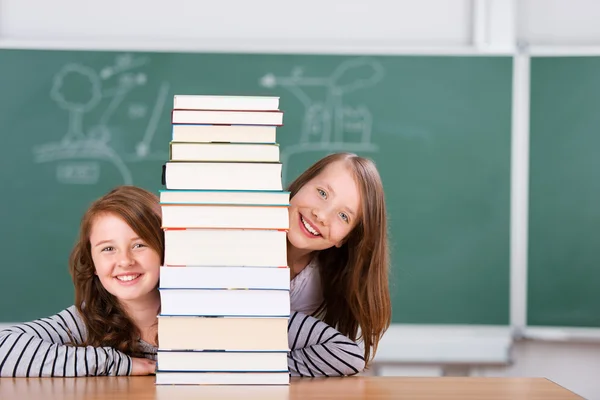 Schoolmeisjes gluren achter een stapel boeken — Stockfoto
