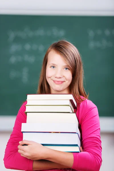 Souriant jeune écolière tenant une pile de livres — Photo