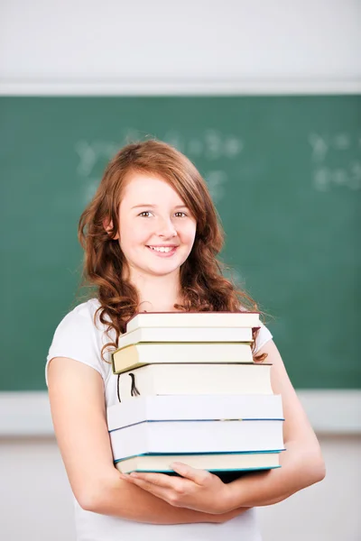 Lächelnde junge Schülerin mit einem Stapel Bücher — Stockfoto